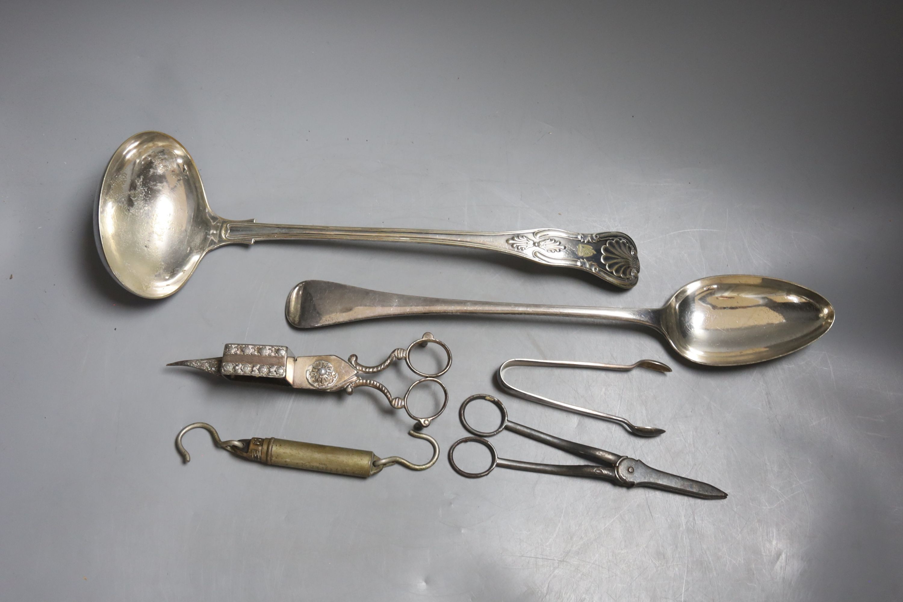 A large plated ladle and basting spoon, two candle snuffers, tongs and spring balance